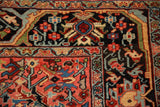 Intricate corner of a Persian Heriz rug with a navy border and colorful blush-red field.