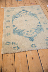Distressed Oushak rug corner: faded sky blue motifs, beige ground, textured pile and fringe.