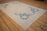 Textured low pile of a distressed Oushak carpet highlighting the cobalt blue corner spandrels on an ivory field.