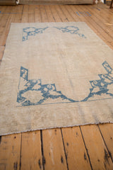 Angled view of a distressed Oushak rug showing its worn, low-pile texture and blue corner spandrels.
