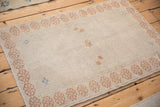 Angled view of a small Oushak rug, its distressed ivory pile and pale copper border.