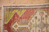 Distressed Oushak rug corner with geometric stepped patterns in terra cotta, lime, and ivory.