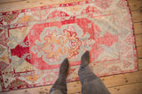 Distressed Oushak rug with soft cinnabar red and ivory hues; feet on pile.