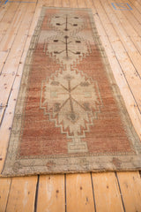 Angled view of distressed vintage Oushak runner in muted copper, sand, and dark motifs.