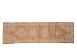 Distressed Oushak runner in muted copper, ivory, and sand with quatrefoil and vine motifs.