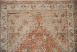 Distressed Oushak rug texture revealing geometric patterns in faded copper and sandy beige.