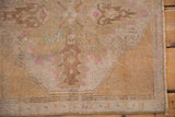 Distressed Oushak rug, machine-bound edge, with worn sand, gold, and pink pattern.