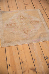 Distressed sand and pale pink Oushak rug corner with machine-bound edge and faded vine design.