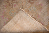 Machine bound side and distressed sand-toned Oushak rug pile with pink marks and scattered white knots.