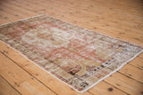 Distressed vintage Oushak rug's time-softened blush, ivory, and brown pattern seen from an angled view.