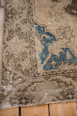 Distressed Oushak rug corner with worn pile, faded brown hues, blue quatrefoil motifs, and machine bound side.