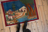 Angled view of a pictorial Kashan rug with a town, trees, and mountain scene.