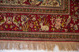 Close-up on an antique Isfahan rug's pictorial border with a rabbit and birds on its cochineal red field.