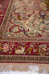 A woven rabbit sits among flowers in the cochineal red border of a fine antique Isfahan rug.