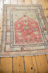 Perspective view of a distressed Turkish Oushak rug highlighting its raspberry red prayer design and geometric borders.