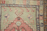 Evenly worn hand-knotted pile showing geometric motifs in blush and jade green.