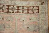 Detail of a distressed Oushak corner showing the chocolate brown geometric border and low-pile texture.