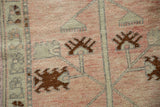 Close-up of the hand-knotted pile showing chocolate brown palmettes and silver vines on a pale rose field.