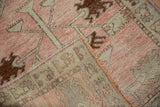 Folded vintage Oushak rug displaying worn blush pile, intact selvage, and woven foundation.