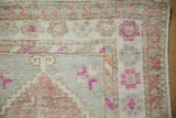 The worn, knotted texture and floral vine border of a vintage distressed Oushak rug corner.