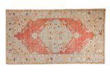 Distressed vintage Oushak rug with a large floral medallion in dusty blue on a faded, abrashed cherry red field.