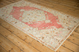 Angled view showcasing the faded cherry red and pale blue floral design of a distressed Oushak rug.