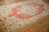 Angled view of a distressed Oushak rug showing its faded cherry red field and pale blue border.