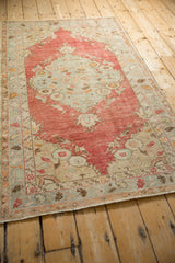 Angled view of a vintage Oushak rug with a large, faded cherry red and blue medallion.
