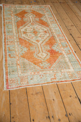 Angled view of a distressed Turkish Oushak runner with rust orange and powder blue geometric patterns.