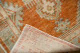 Folded corner of a distressed Oushak rug showing its tangerine orange low pile and hand-knotted back.
