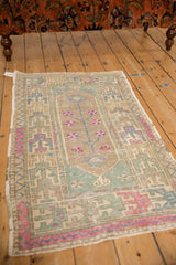 Angled view of a small distressed Oushak rug with a tree of life motif in faded pastels.