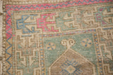 Detail of the distressed Turkish Oushak's corner spandrel with pinwheel motifs in fuchsia and mint.