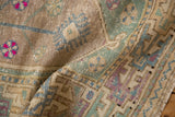 Textured low pile of a distressed Oushak rug with dusty mint green and fuchsia accents.