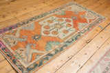Distressed Oushak runner's primitive arabesque border with rust, seafoam, and magenta tones.