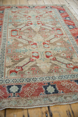 Distressed Anatolian rug's geometric pattern in red, blue, and coffee brown, seen from an angle.