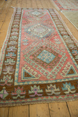 Angled view of distressed Oushak runner's bronze border and blush, blue geometric patterns with wear.