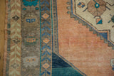 Corner view of a distressed Oushak rug with finned vine and floral border motifs.