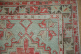 Geometric borders of a distressed Oushak rug in faded cherry red, brown, and seafoam green.