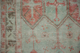 Low-pile texture of a distressed Oushak showing geometric motifs in faded red and seafoam green.