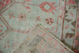 Folded corner of a distressed Oushak rug reveals the hand-knotted weave and low pile texture.
