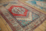 Distressed vintage Anatolian rug from an angle, highlighting its ruby red medallion and teal geometric field.