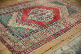 Angled perspective on a distressed Anatolian rug highlighting its abrashed ruby red field and teal corners.