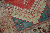 Stylized trident blossoms and stepped contours in red, teal, and beige on a distressed Anatolian rug.