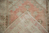 Distressed pile of a vintage Oushak rug in pale tones, folded to reveal its hand-knotted reverse.