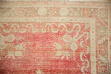 Low-pile texture showing knot heads on the cherry red field and ivory border of a distressed Oushak rug.