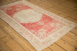 An angled view highlighting the decorative distressed wear on a vintage red and ivory Turkish Oushak rug.