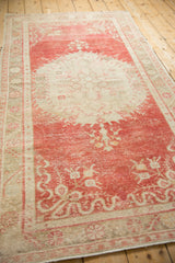 A vintage Oushak rug from an angle, highlighting its time-softened cherry red and ivory design.