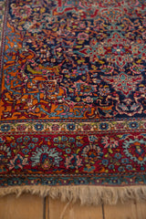 Corner detail of a collector Kashan rug showing scrolling vines and elaborate floral borders.