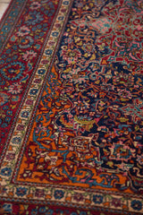 Elaborate cloudband motifs and sprawling vines in tangerine, ruby, and navy on a collector Kashan rug.