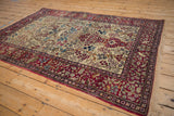 Angled view of an antique Isfahan rug's pictorial ivory field and intricate cochineal red border.